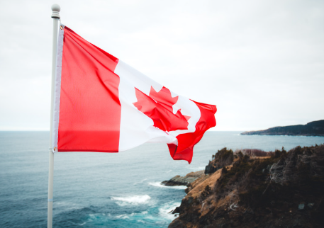 An image showing the Canadian flag blowing in the wind near bluffs, to represent the journey of Immigrating to Canada.